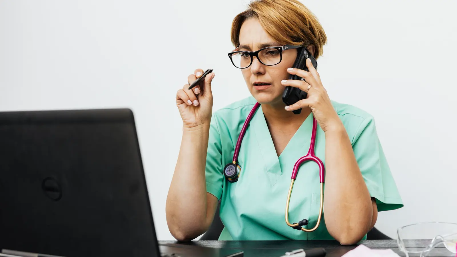 Clinician in scrubs working at a laptop in a bright clinical room