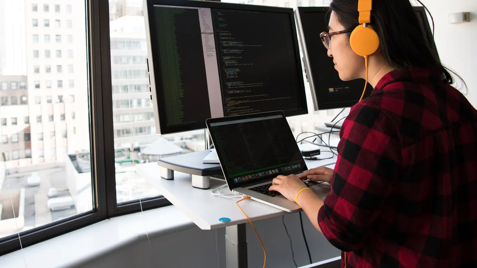 A software engineer working at a laptop beside an office window