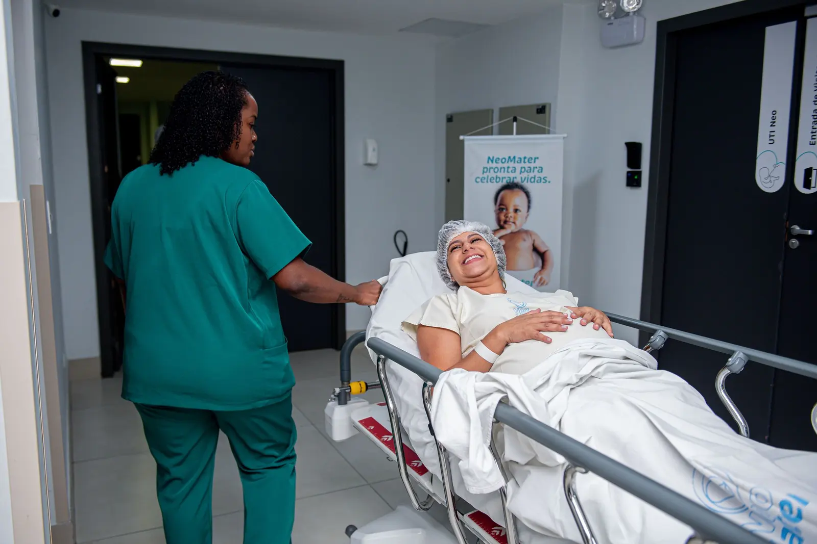 Nurse in green scrubs wheeling a patient in a hospital bed down a corridor